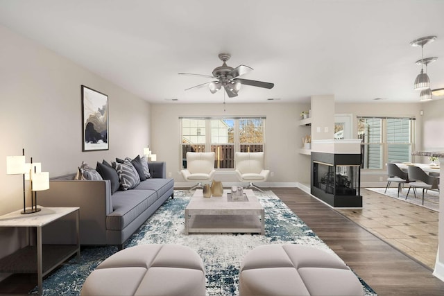 living room with a multi sided fireplace, dark hardwood / wood-style floors, and ceiling fan