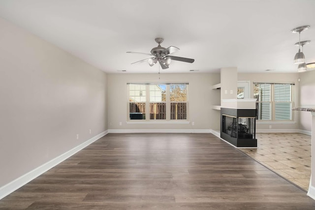 unfurnished living room with ceiling fan, a multi sided fireplace, and dark tile patterned floors