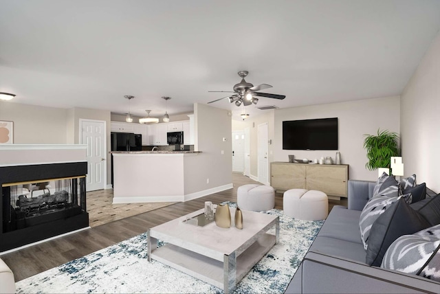 living room with hardwood / wood-style flooring, ceiling fan, and a multi sided fireplace