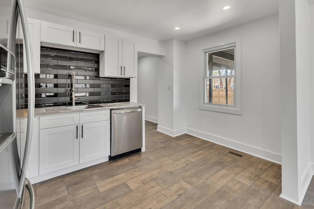 kitchen featuring light stone countertops, white cabinets, stainless steel appliances, decorative backsplash, and sink