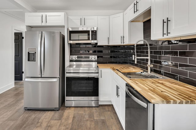 kitchen featuring appliances with stainless steel finishes, white cabinetry, sink, backsplash, and butcher block countertops