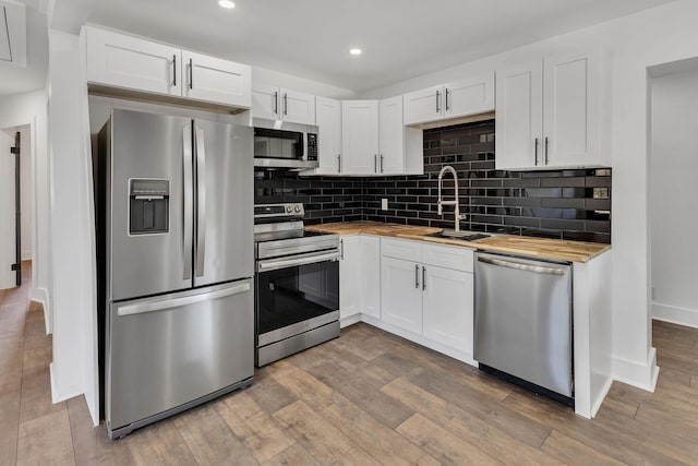 kitchen with light hardwood / wood-style flooring, appliances with stainless steel finishes, sink, white cabinets, and butcher block countertops