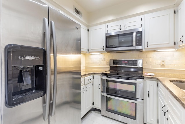 kitchen with white cabinetry, stainless steel appliances, backsplash, light tile patterned flooring, and light stone counters