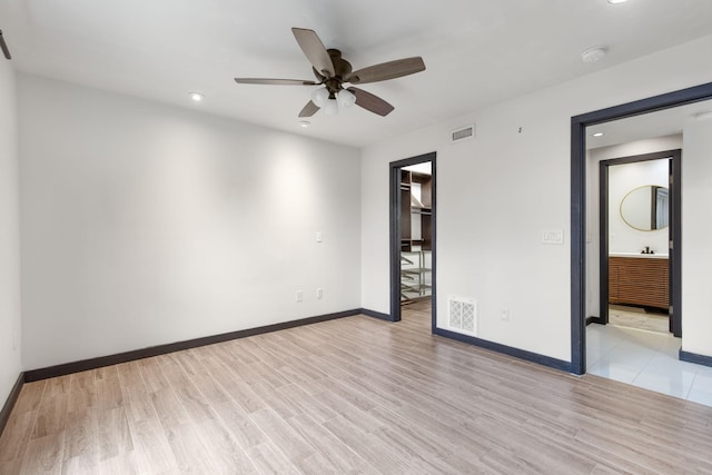 unfurnished bedroom with a walk in closet, ceiling fan, light wood-type flooring, and a closet