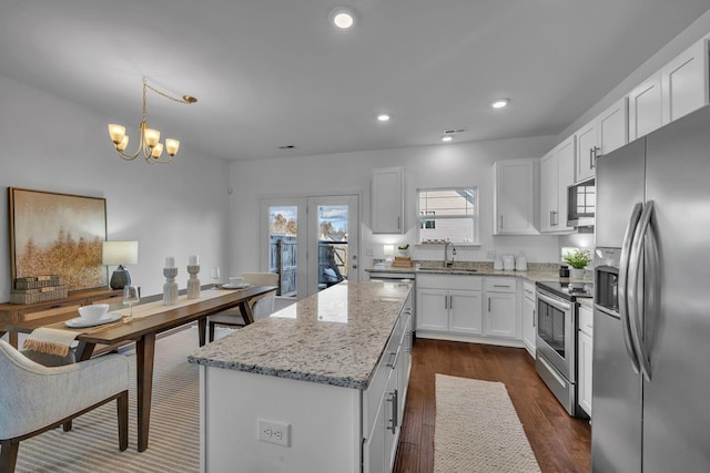 kitchen featuring pendant lighting, appliances with stainless steel finishes, white cabinetry, light stone countertops, and a center island