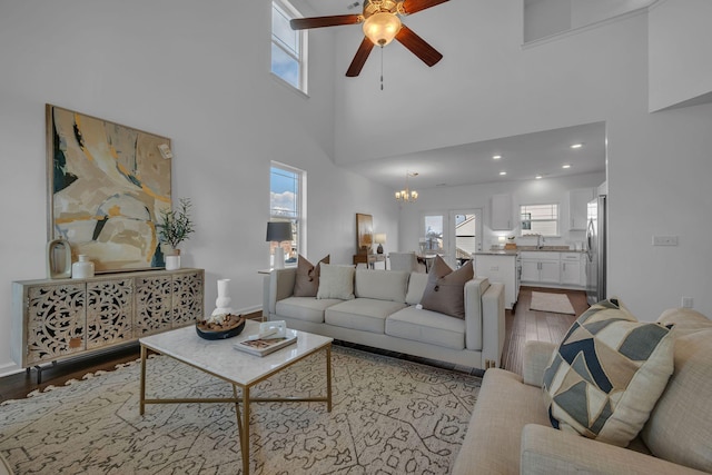 living room with sink, a towering ceiling, ceiling fan with notable chandelier, and light hardwood / wood-style flooring