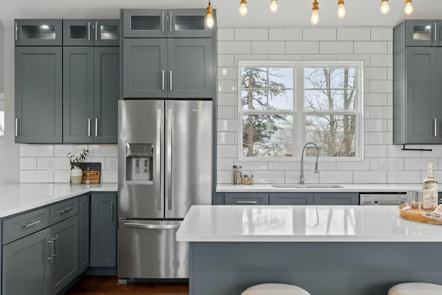 kitchen featuring sink, backsplash, stainless steel fridge, hanging light fixtures, and a breakfast bar