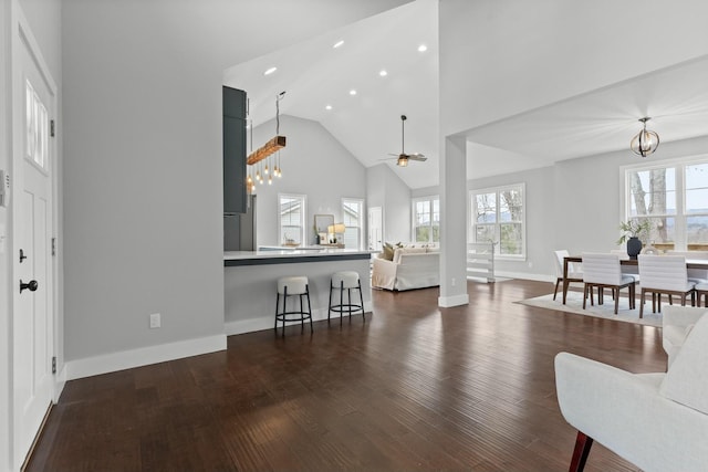 living room with dark wood-type flooring, ceiling fan with notable chandelier, and high vaulted ceiling