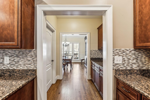 kitchen featuring a chandelier, backsplash, dark hardwood / wood-style floors, and dark stone counters