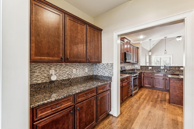 kitchen featuring decorative light fixtures, stainless steel appliances, dark stone counters, light hardwood / wood-style floors, and sink