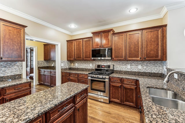 kitchen featuring crown molding, appliances with stainless steel finishes, sink, light wood-type flooring, and dark stone countertops