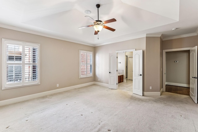 unfurnished bedroom featuring ceiling fan, a raised ceiling, light colored carpet, ensuite bath, and ornamental molding