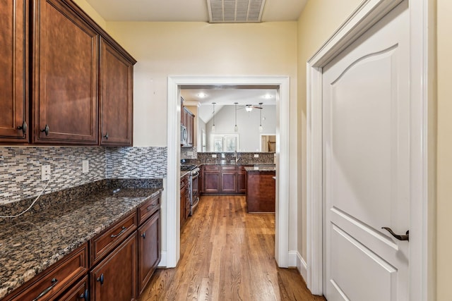 kitchen featuring stainless steel appliances, dark stone countertops, light hardwood / wood-style floors, sink, and backsplash