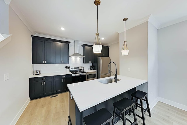 kitchen featuring hanging light fixtures, wall chimney exhaust hood, sink, a breakfast bar, and stainless steel appliances