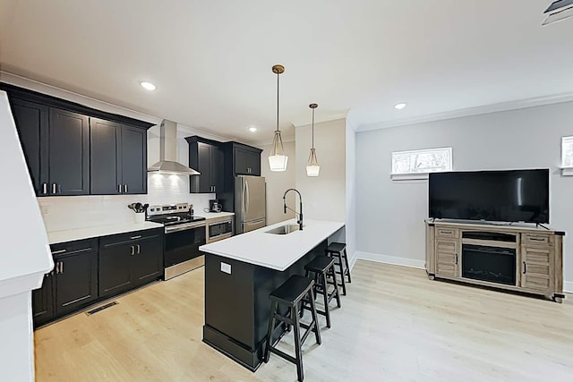 kitchen featuring wall chimney exhaust hood, sink, a kitchen island with sink, a breakfast bar, and stainless steel appliances