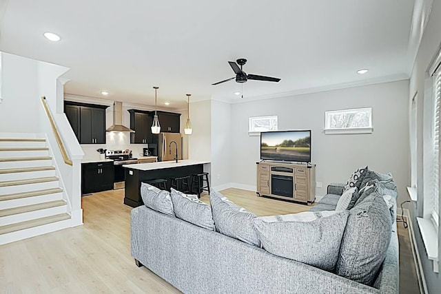 living room featuring light wood-type flooring, ceiling fan, ornamental molding, and sink