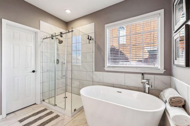 bathroom with a wealth of natural light, tile walls, and separate shower and tub