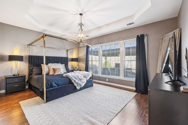 bedroom with dark hardwood / wood-style flooring, a raised ceiling, and an inviting chandelier