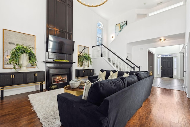 living room with a towering ceiling, dark hardwood / wood-style floors, and a large fireplace