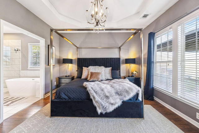 bedroom with an inviting chandelier, dark wood-type flooring, and a tray ceiling