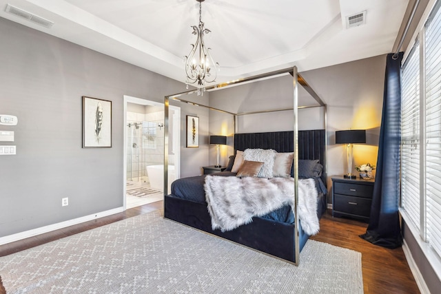 bedroom with ensuite bath, dark hardwood / wood-style floors, a raised ceiling, and a notable chandelier