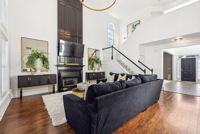 living room with a high ceiling, dark hardwood / wood-style floors, an inviting chandelier, and a fireplace