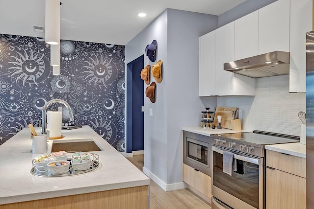 kitchen featuring white cabinets, stainless steel appliances, tasteful backsplash, sink, and light wood-type flooring