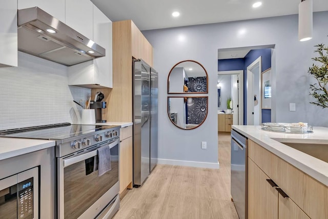 kitchen featuring light brown cabinetry, light hardwood / wood-style floors, appliances with stainless steel finishes, white cabinets, and backsplash