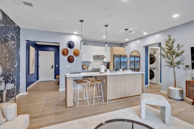 kitchen with white cabinetry, stacked washer / dryer, a kitchen island with sink, and pendant lighting