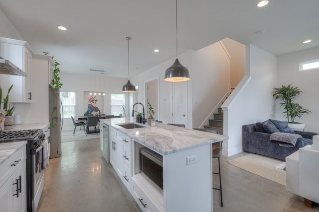 kitchen featuring decorative light fixtures, white cabinetry, stainless steel appliances, an island with sink, and sink