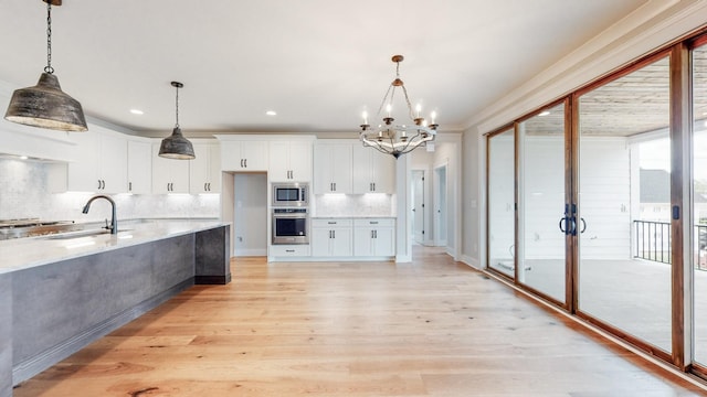 kitchen with appliances with stainless steel finishes, decorative light fixtures, sink, white cabinets, and light hardwood / wood-style floors