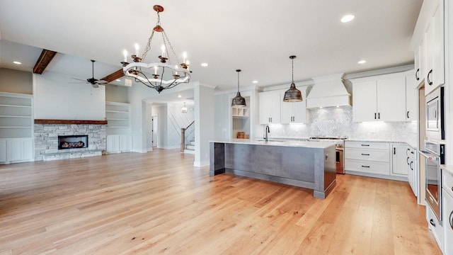 kitchen with white cabinets, stainless steel appliances, custom range hood, and a center island with sink