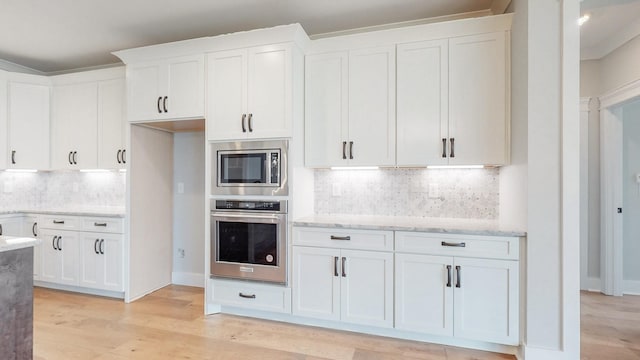 kitchen with light stone countertops, appliances with stainless steel finishes, white cabinetry, decorative backsplash, and light hardwood / wood-style flooring