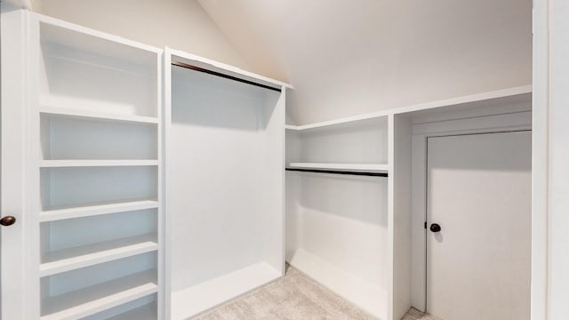 walk in closet with light colored carpet and vaulted ceiling