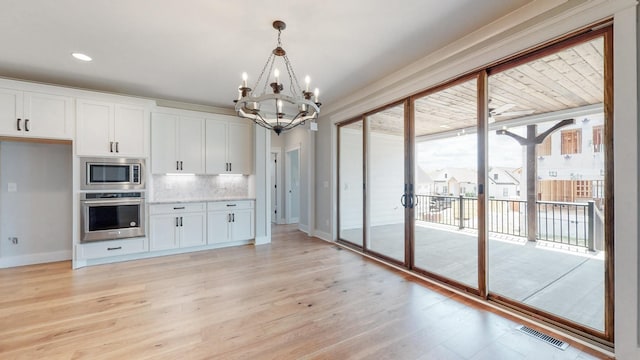 kitchen with white cabinets, stainless steel appliances, decorative backsplash, hanging light fixtures, and light hardwood / wood-style flooring