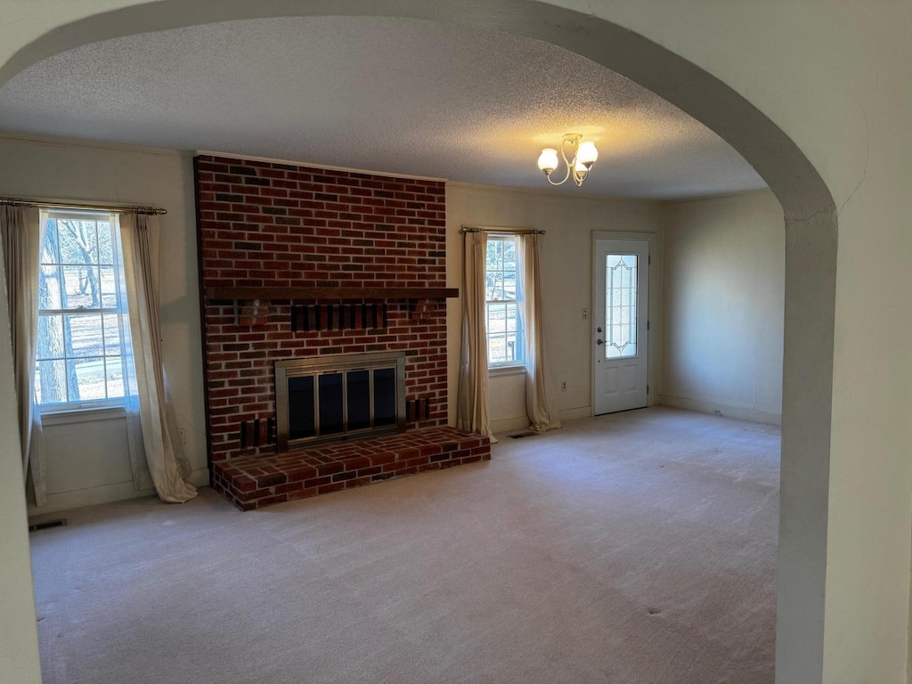 unfurnished living room with a textured ceiling, carpet floors, and a brick fireplace