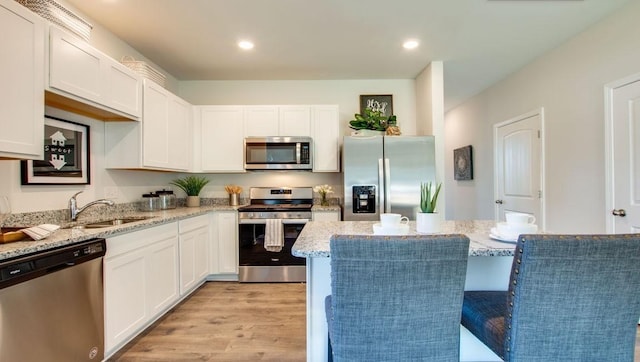 kitchen featuring white cabinets, light hardwood / wood-style floors, light stone counters, and appliances with stainless steel finishes