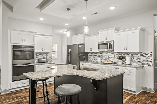 kitchen with light stone countertops, sink, white cabinets, decorative light fixtures, and stainless steel appliances