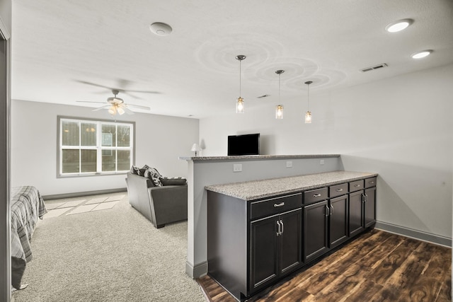 kitchen with light stone countertops, kitchen peninsula, pendant lighting, dark hardwood / wood-style flooring, and ceiling fan