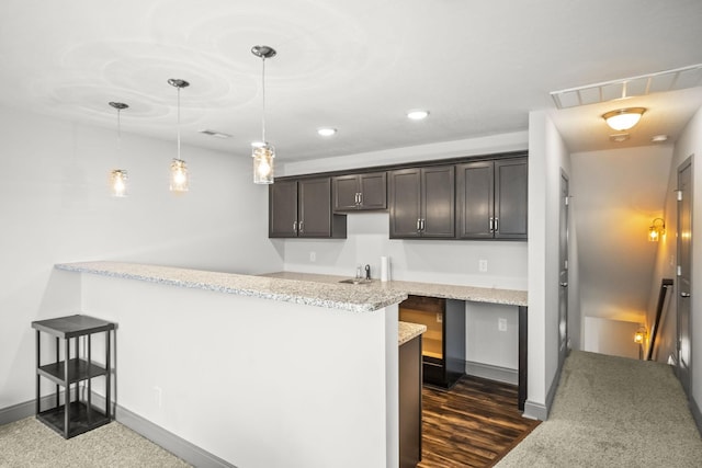 kitchen featuring light stone countertops, dark brown cabinetry, kitchen peninsula, and pendant lighting