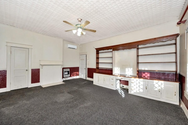 unfurnished living room featuring an AC wall unit, built in desk, dark colored carpet, ceiling fan, and heating unit