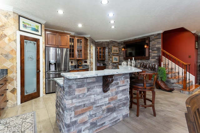 kitchen featuring light stone counters, a center island, ornamental molding, stainless steel fridge, and a kitchen breakfast bar