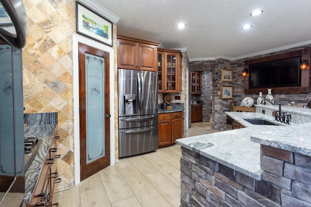 kitchen featuring stainless steel refrigerator with ice dispenser, crown molding, sink, and light stone counters