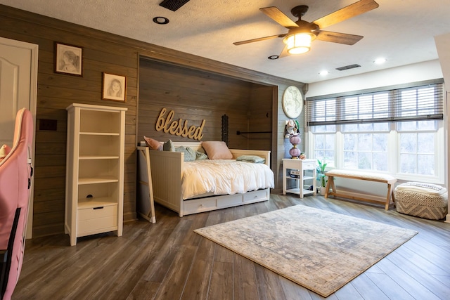 bedroom featuring ceiling fan, wooden walls, dark hardwood / wood-style flooring, and a textured ceiling