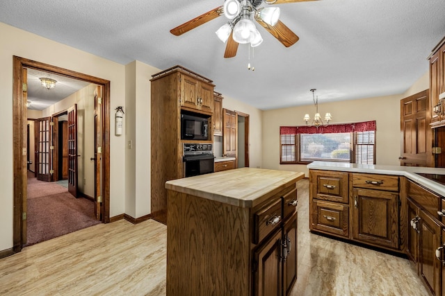 kitchen with black appliances, a center island, a textured ceiling, hanging light fixtures, and wooden counters