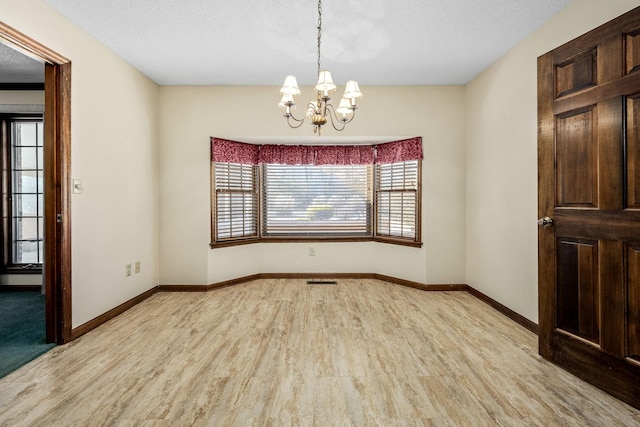 spare room with light hardwood / wood-style floors, a textured ceiling, and a notable chandelier