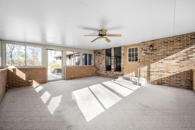 unfurnished living room featuring a wealth of natural light, brick wall, and carpet flooring