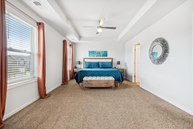 carpeted bedroom with multiple windows, ceiling fan, and a raised ceiling