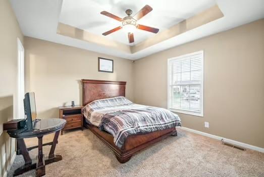 bedroom featuring ceiling fan, light carpet, and a tray ceiling