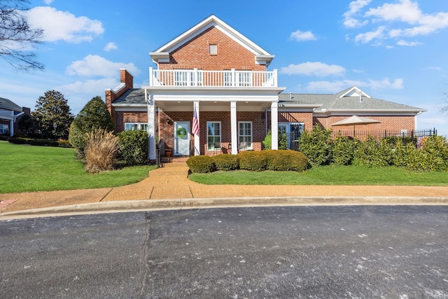 view of front of home featuring a front lawn, a balcony, and covered porch